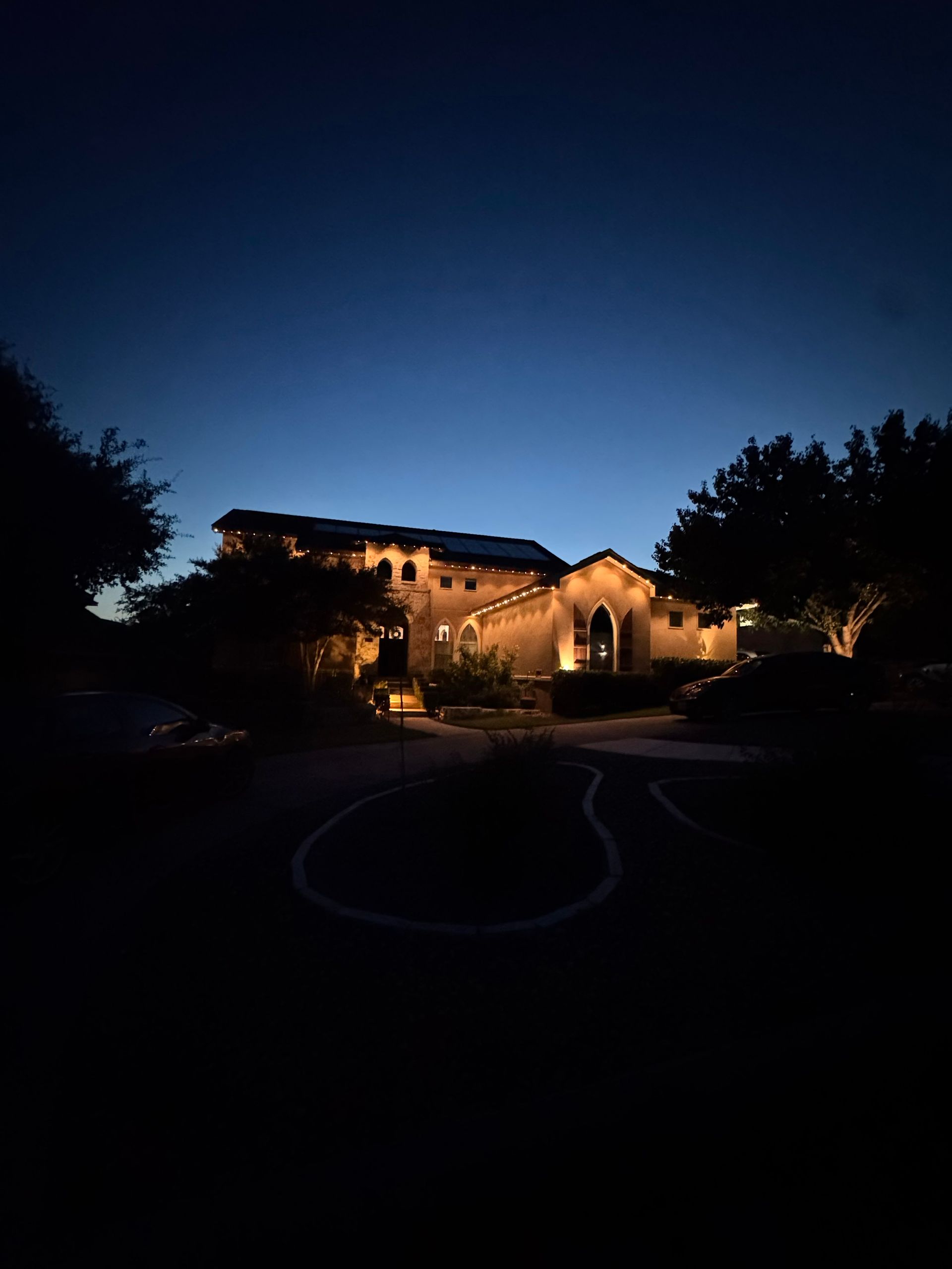 Nighttime view of a lit house with landscaping against a dark blue sky.