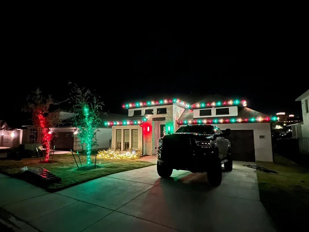 Christmas lights decorate a house at night, with a truck parked in the driveway. Red and green lights.