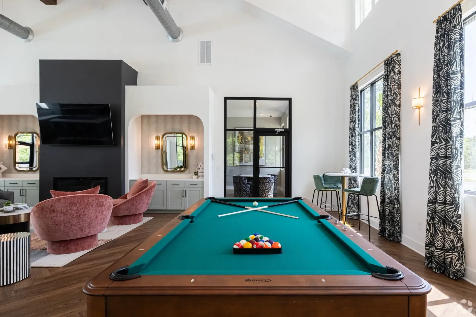 Modern game room with a pool table, pink chairs, large mirrors, and black-and-white curtains