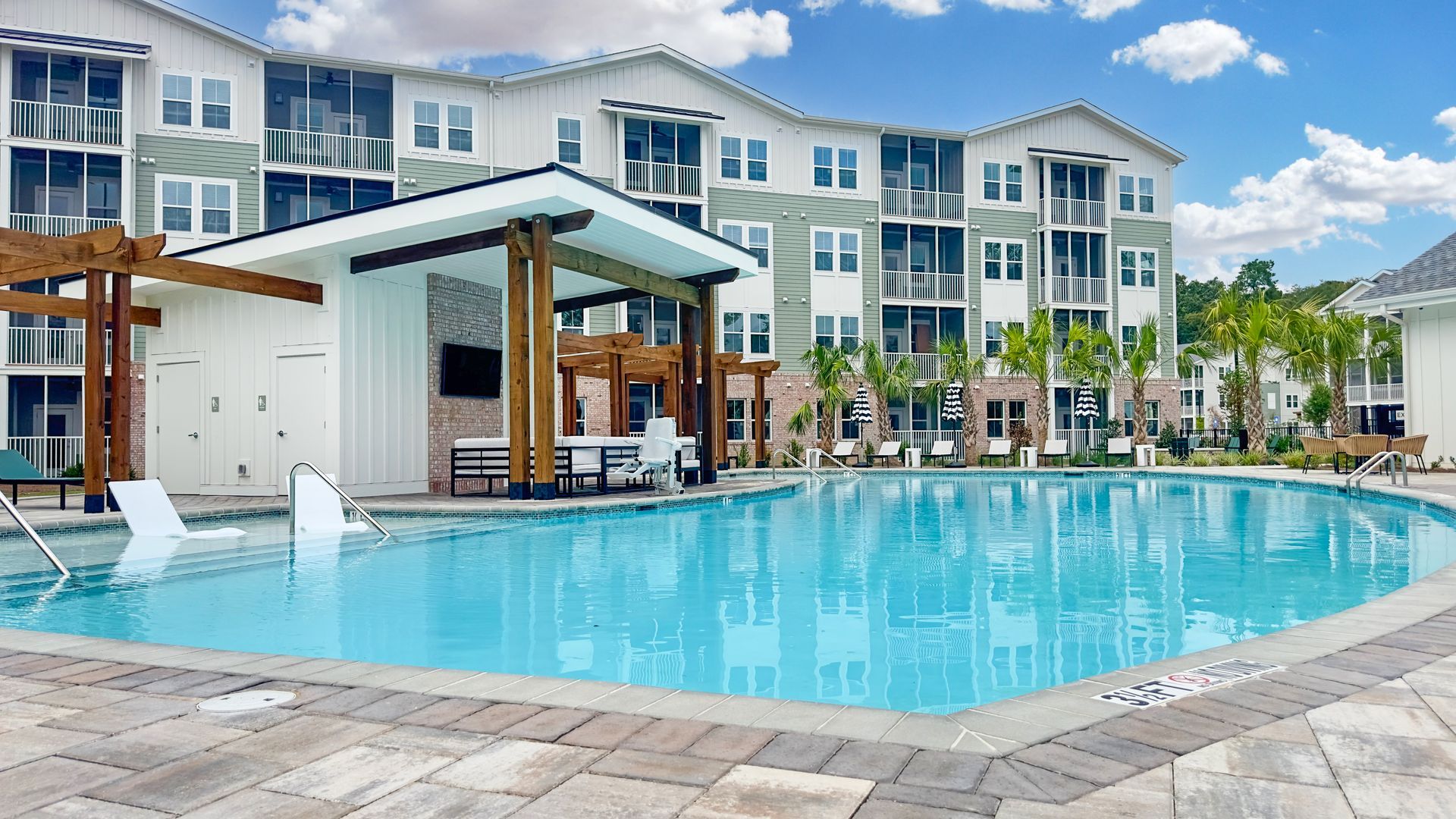 Apartment pool with clear blue water, lounge chairs, and modern multi-story buildings in the background