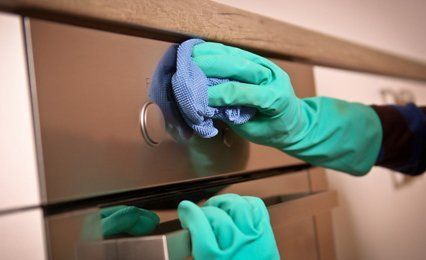 Hands in turquoise rubber gloves polishing a chest of drawers