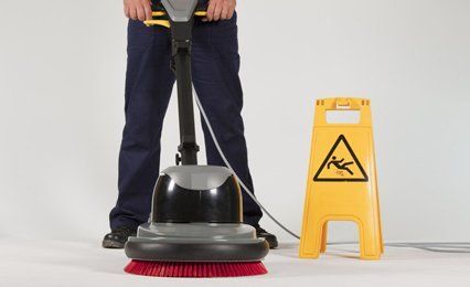 A man using an industrial floor cleaner next to a yellow 