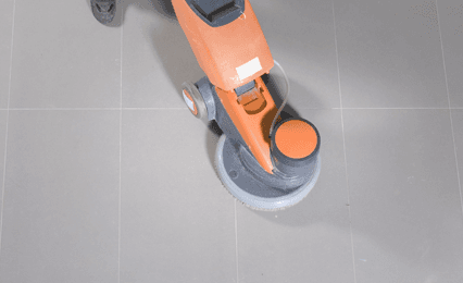 An orange floor cleaner on a grey tiled floor