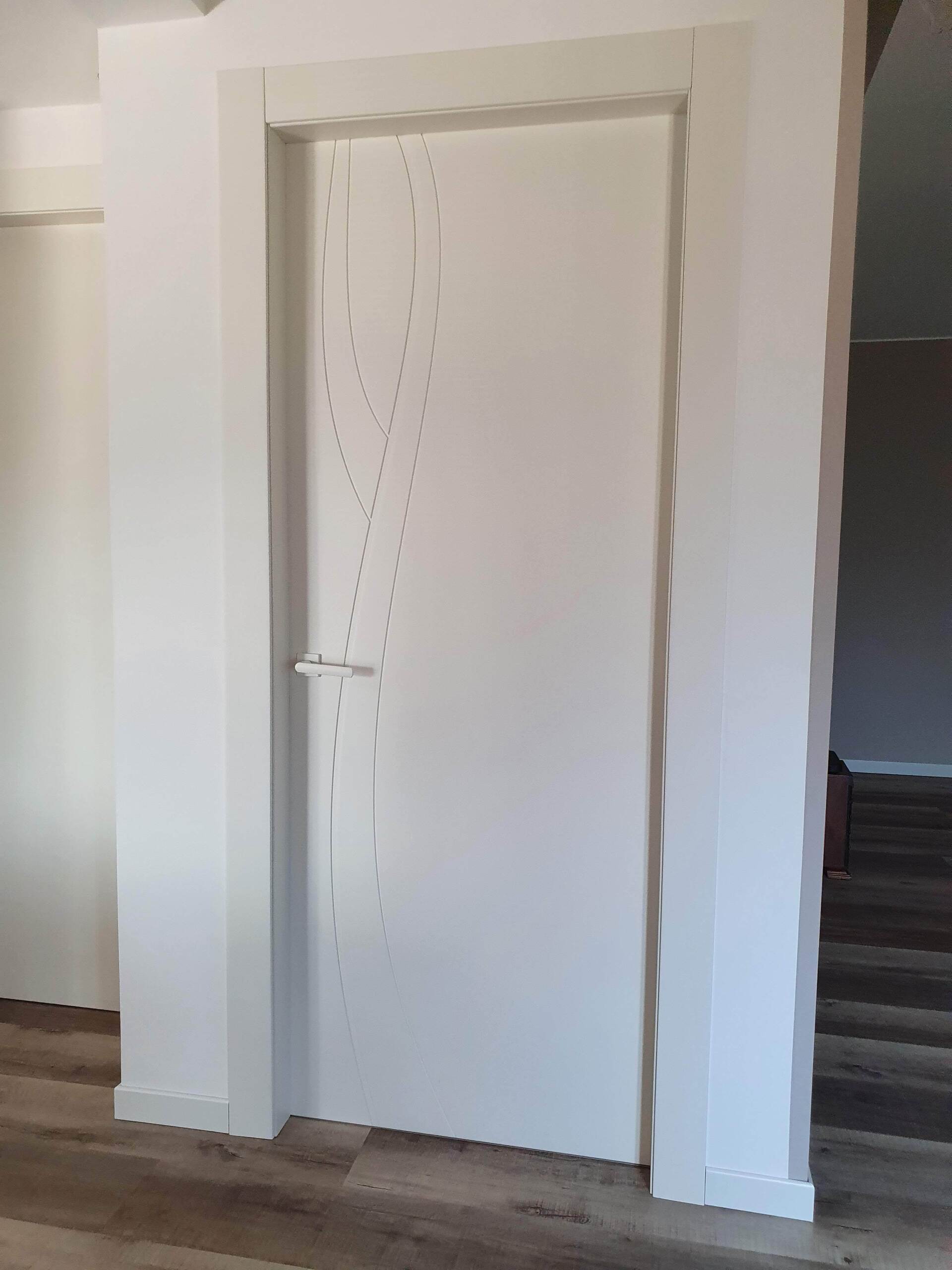 Una porta bianca si trova in una stanza accanto a un pavimento in legno.