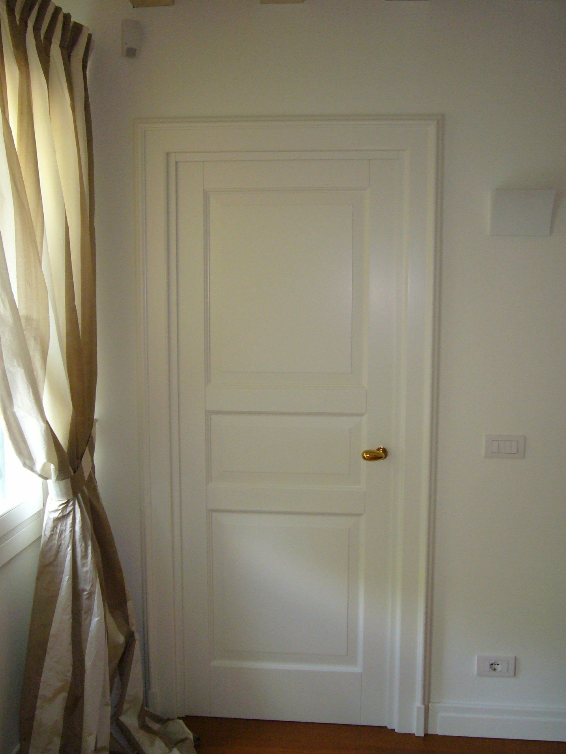 Una porta bianca si trova in una stanza accanto a una finestra.