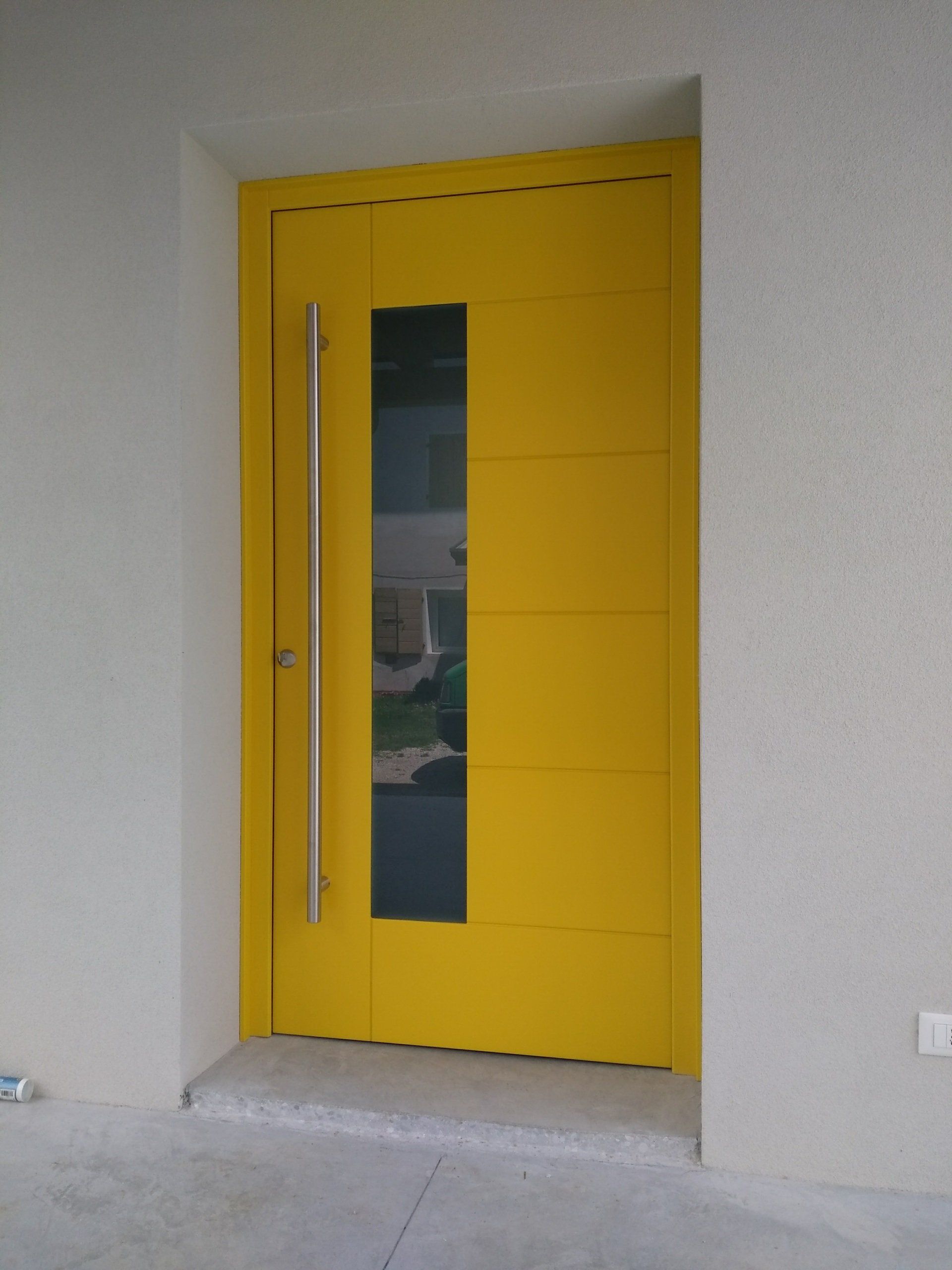 Una porta gialla con una maniglia in acciaio inossidabile si trova su un muro bianco.