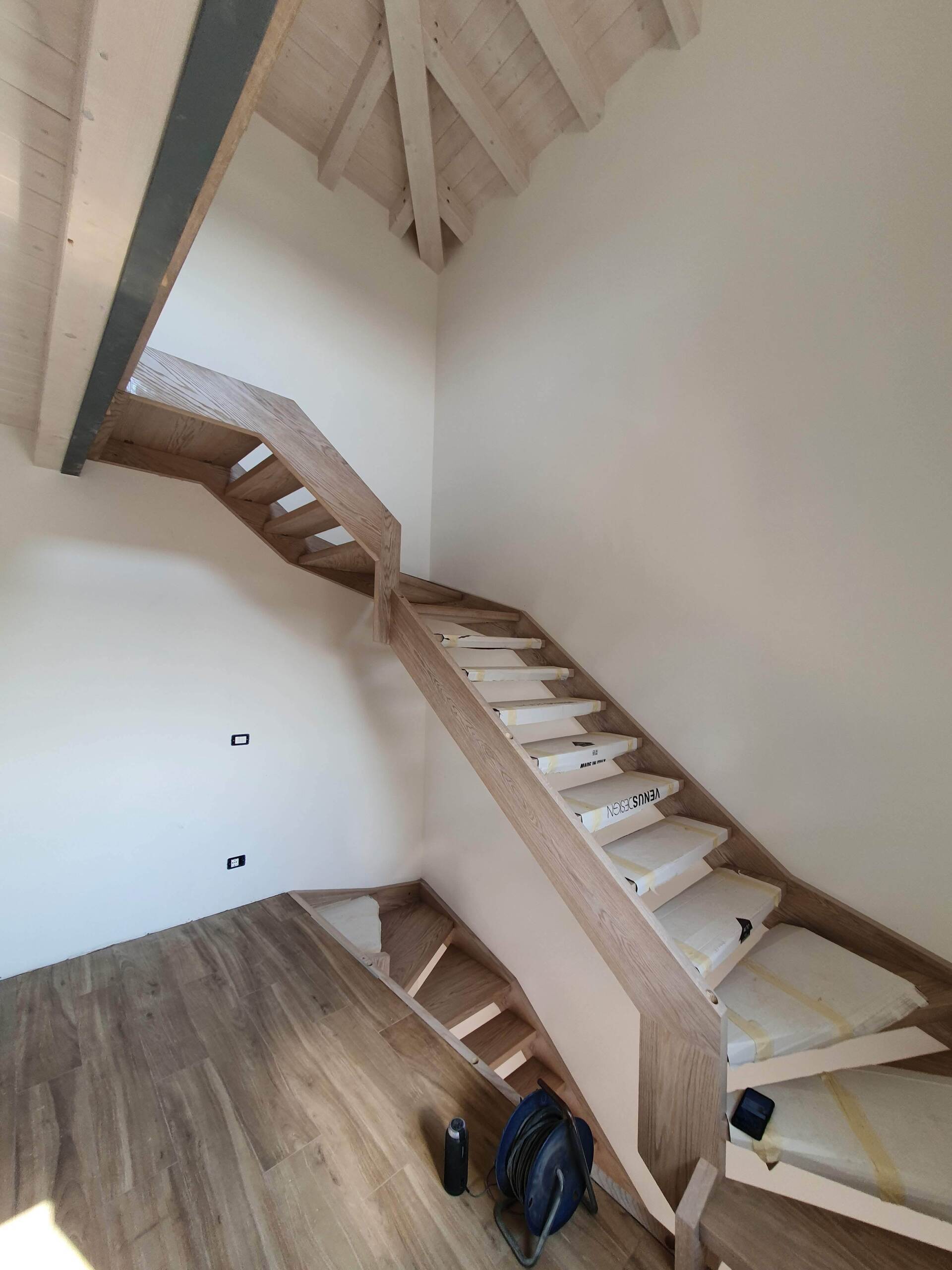 Una scala di legno in una stanza con uno zaino sul pavimento.