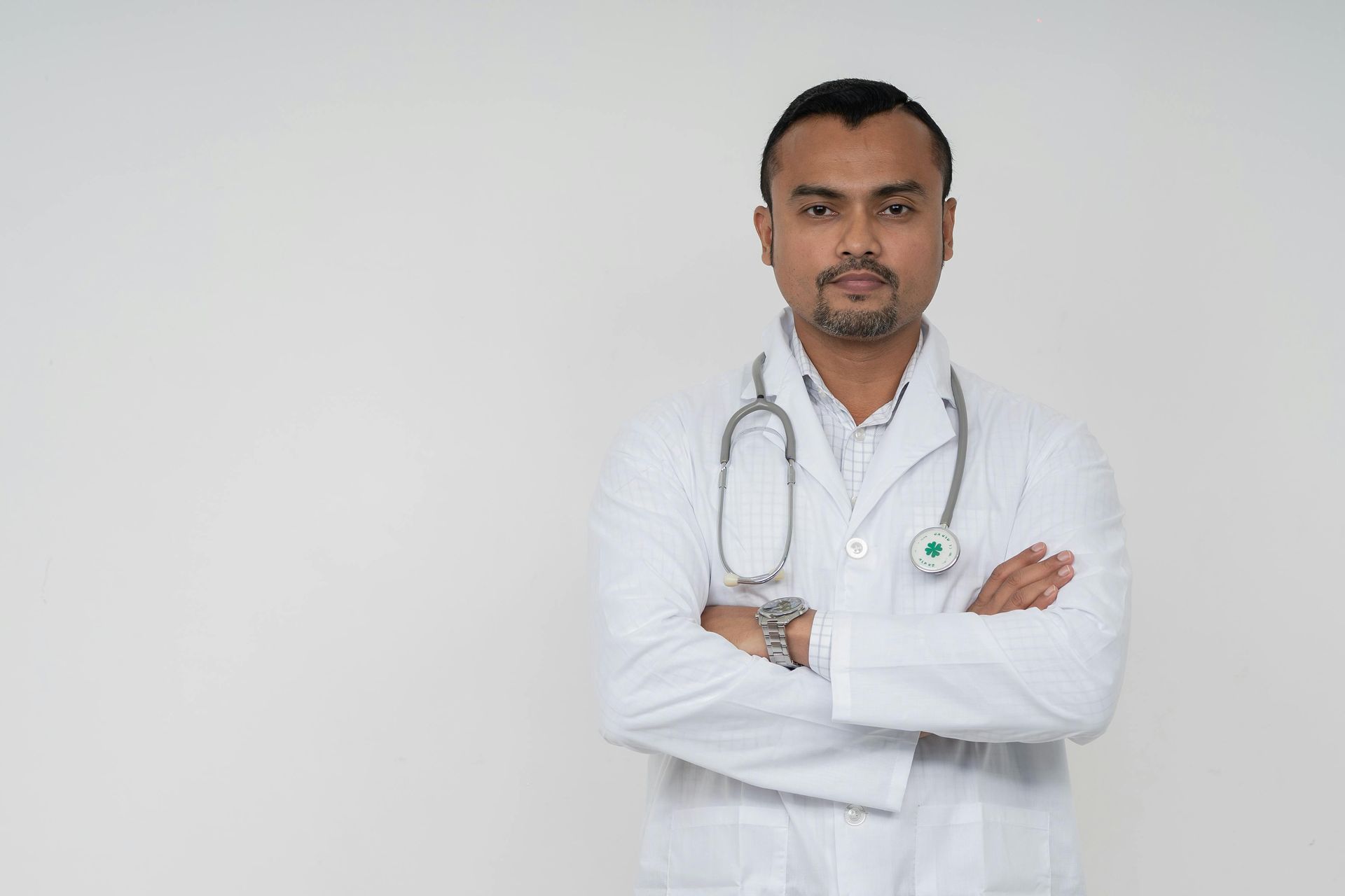 Doctor with arms crossed, wearing a white coat and stethoscope against a white backdrop.
