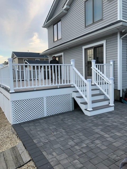 Wooden deck with railing, grill, table, chairs, and umbrella, surrounded by green trees.