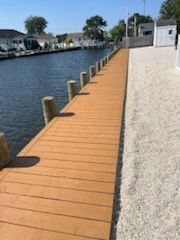 Wooden deck overlooking lush greenery, trees, and a body of water. Bright sunny day.