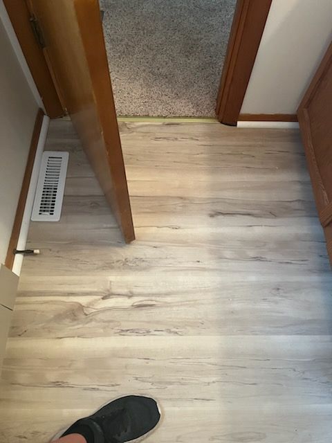 Person installing light-colored wood flooring. The setting is indoors.
