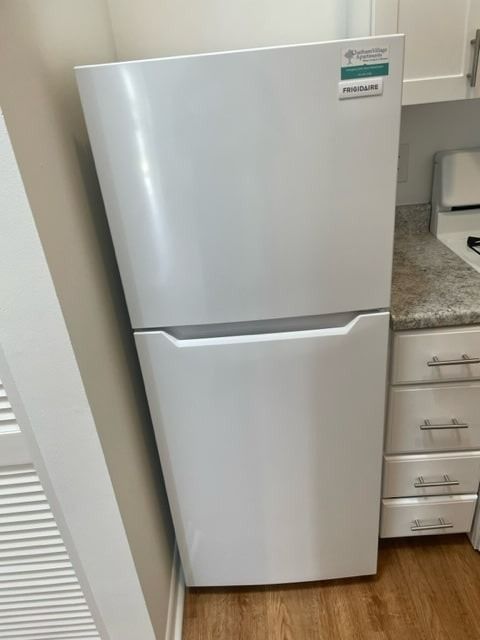 White refrigerator in a kitchen next to a countertop and cabinets.