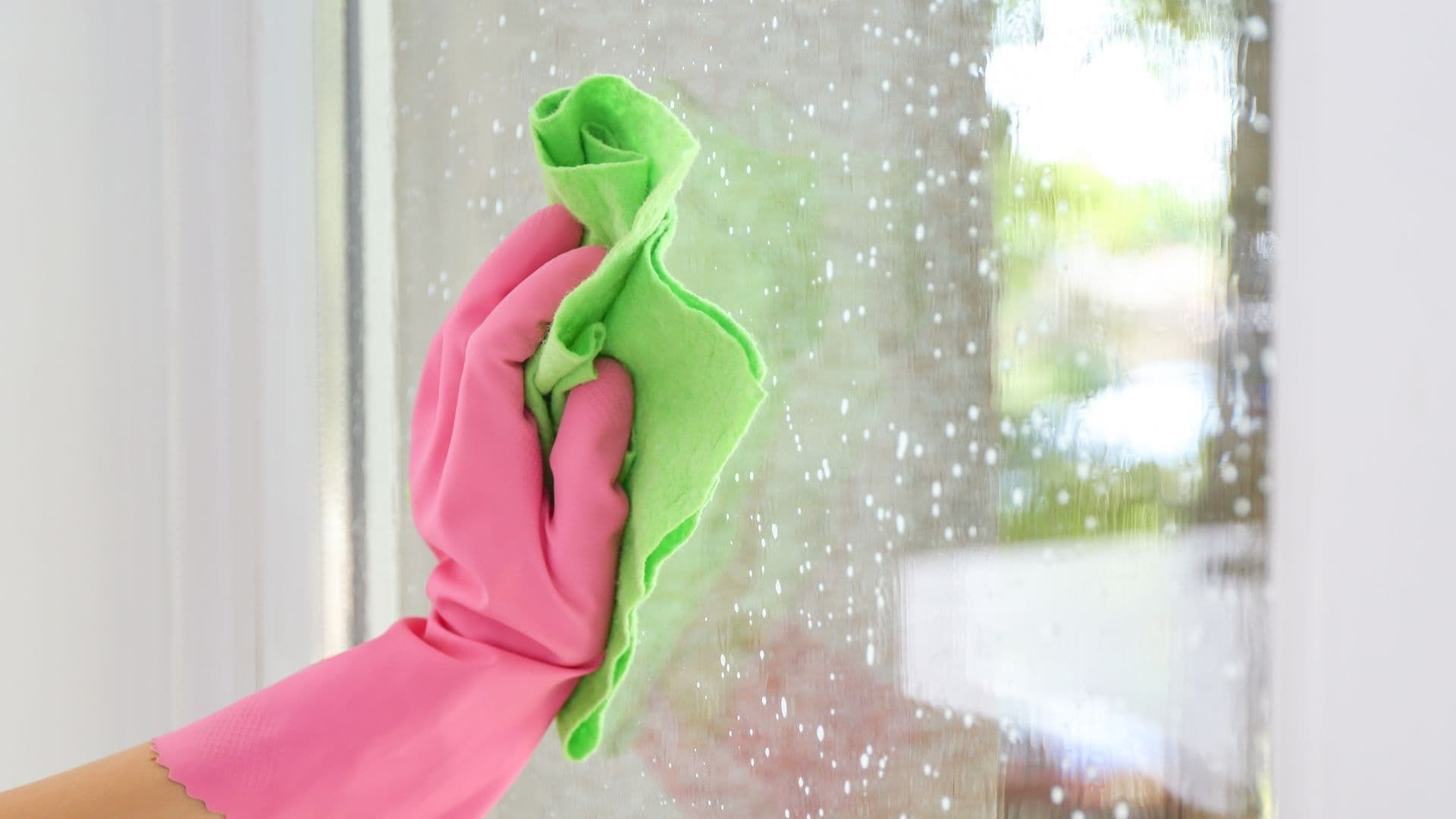 Hand in pink glove wiping a window with a green cloth.