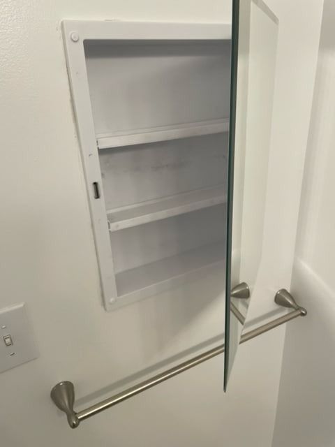 White recessed medicine cabinet with opened mirrored door, attached towel bar.