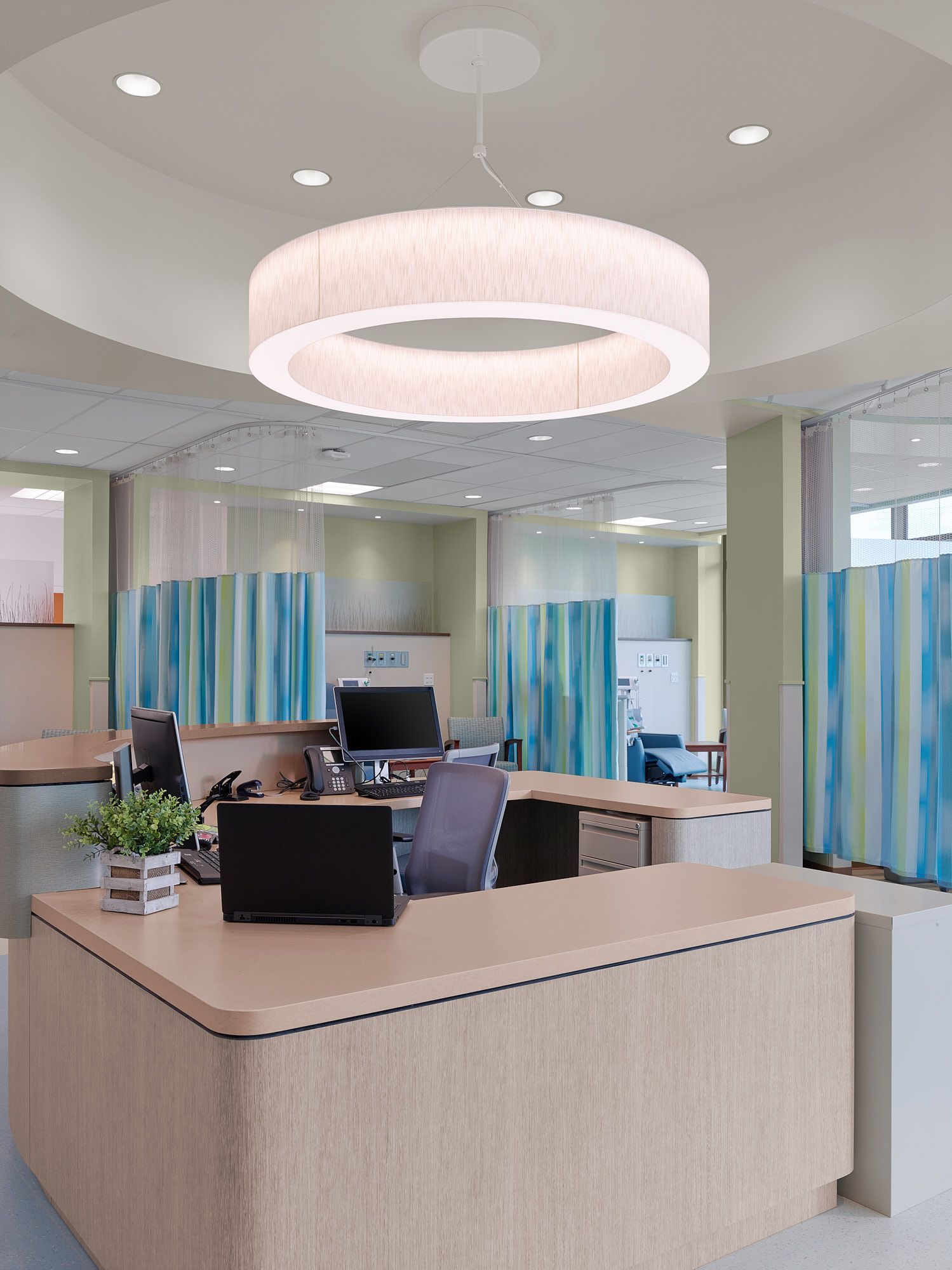 Office area with a large circular light fixture, desks, and teal and blue striped privacy curtains.