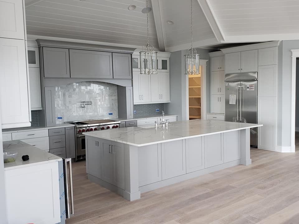 A newly constructed kitchen with gray and white cabinets, a large island, stainless steel appliances, and wood flooring.