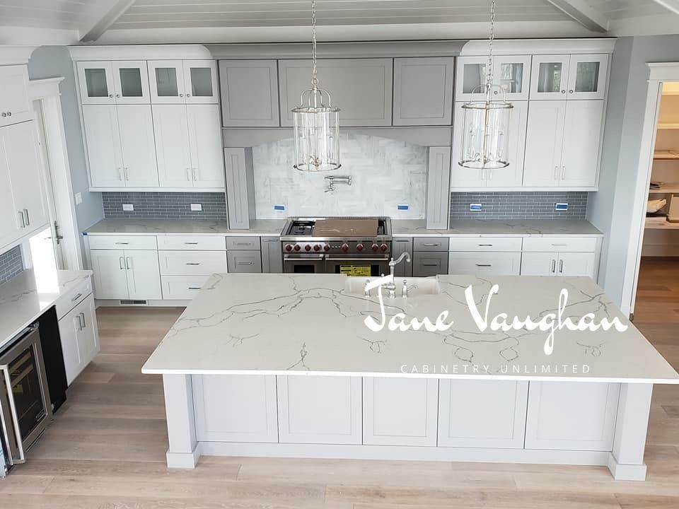 A modern, light-filled kitchen with a large island. Gray and white cabinets, quartz countertops, and a stainless steel range.