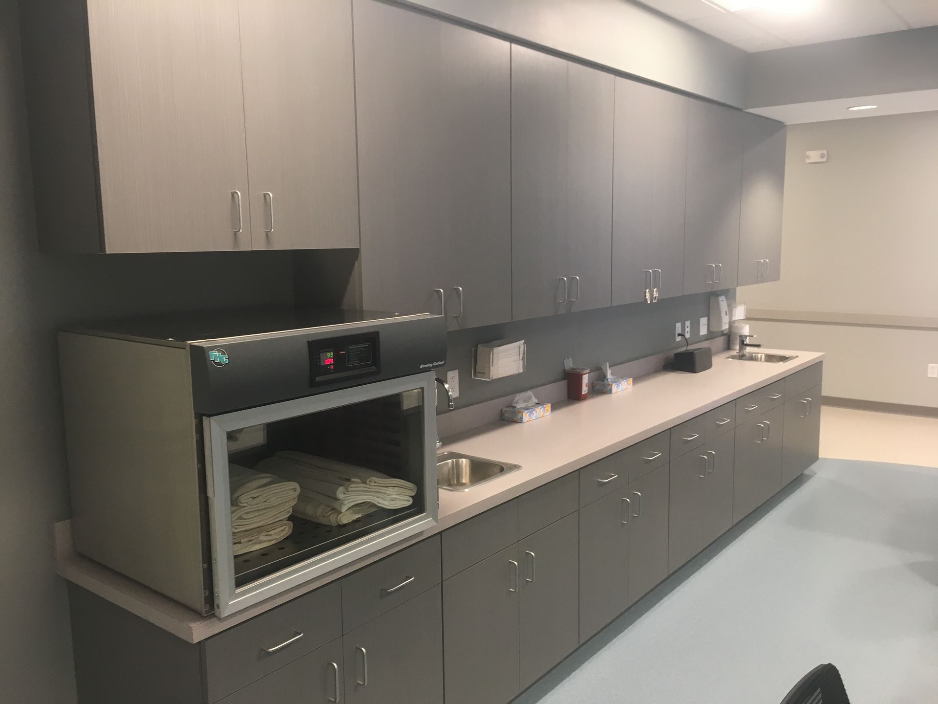 A gray lab space featuring a cabinet, a sterilizer, and a long countertop with cabinets and sinks.