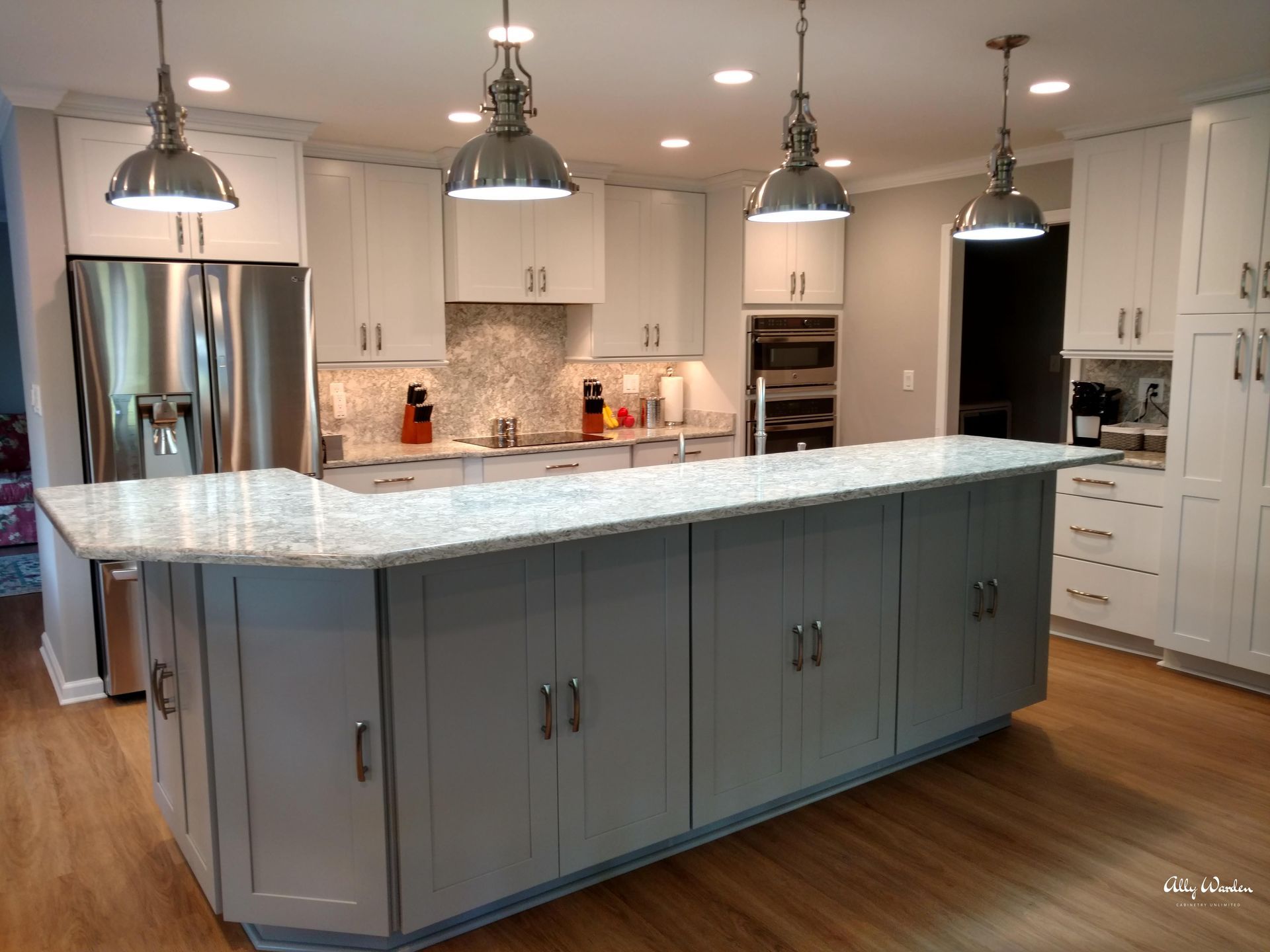A spacious kitchen with a gray island and white cabinets. Stainless steel appliances, pendant lights, and wood flooring complete the design.