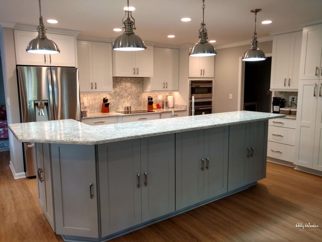 Modern kitchen with gray island and white cabinets, wood floors, stainless steel appliances, and pendant lights.