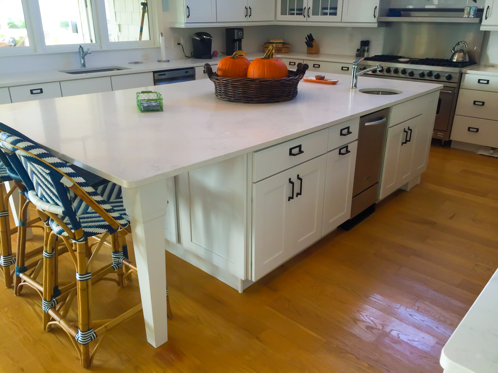 White kitchen island with a marble countertop, a built-in dishwasher and sink, and two blue and white patterned bar stools.
