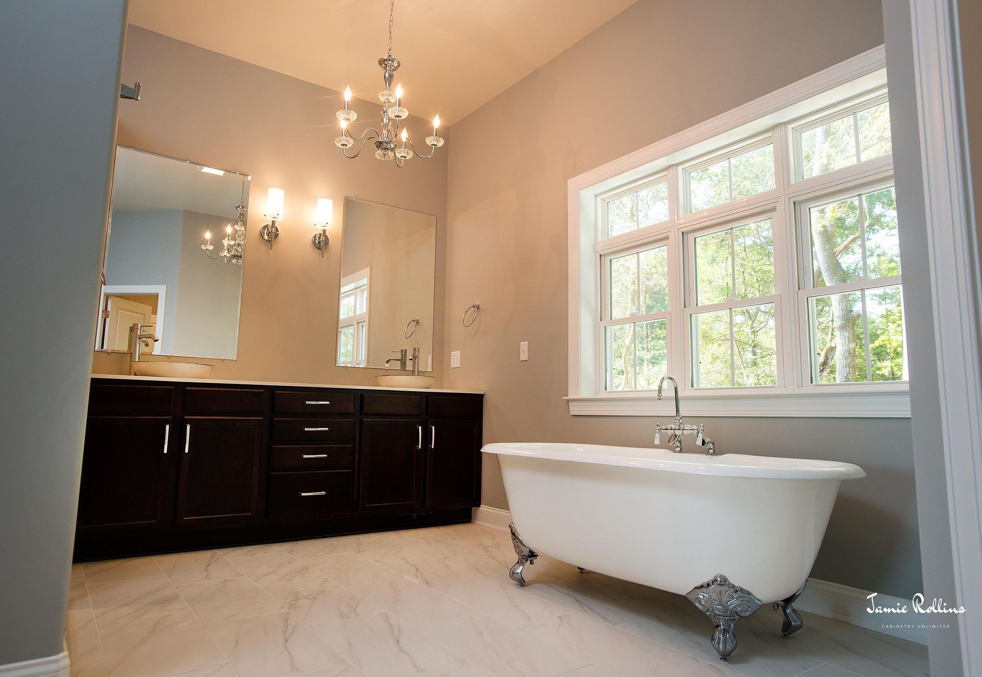 Bathroom with a white clawfoot tub, dark wood vanity, and a large window. A chandelier hangs overhead, and the walls are painted gray.