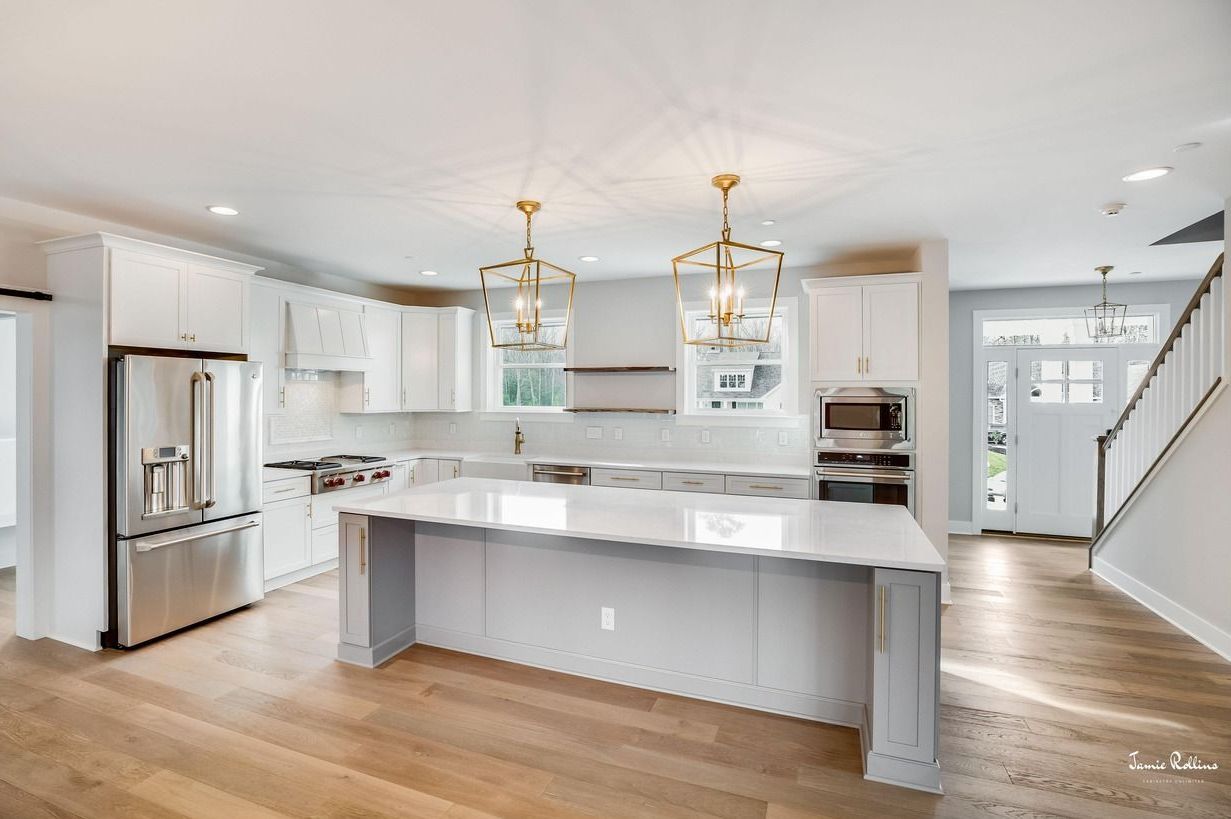 Bright, modern kitchen with white cabinets, island, and stainless steel appliances. Wooden floors and gold pendant lights add warmth.