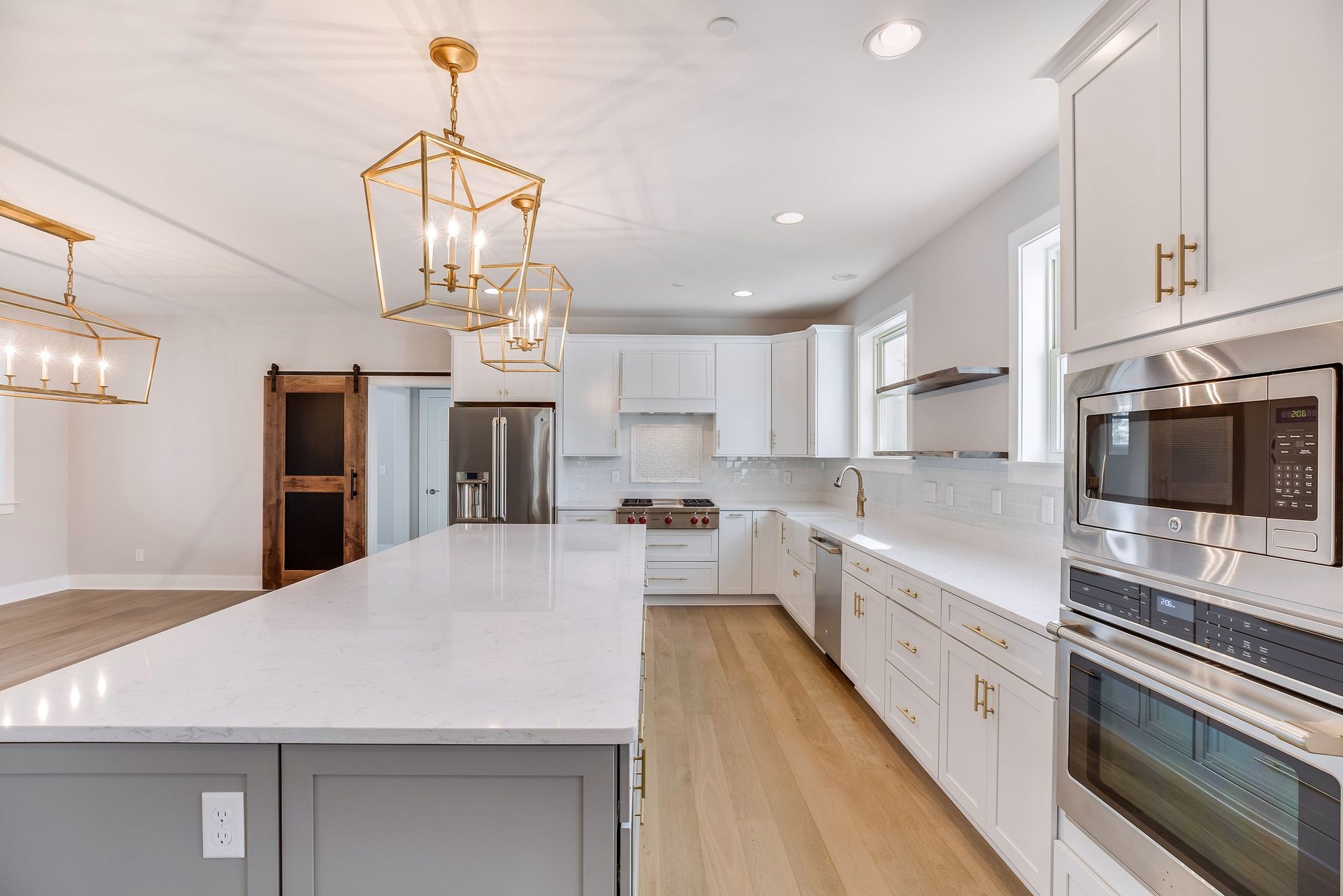 Modern kitchen with white cabinets, large island with gray base, stainless steel appliances, and gold light fixtures.