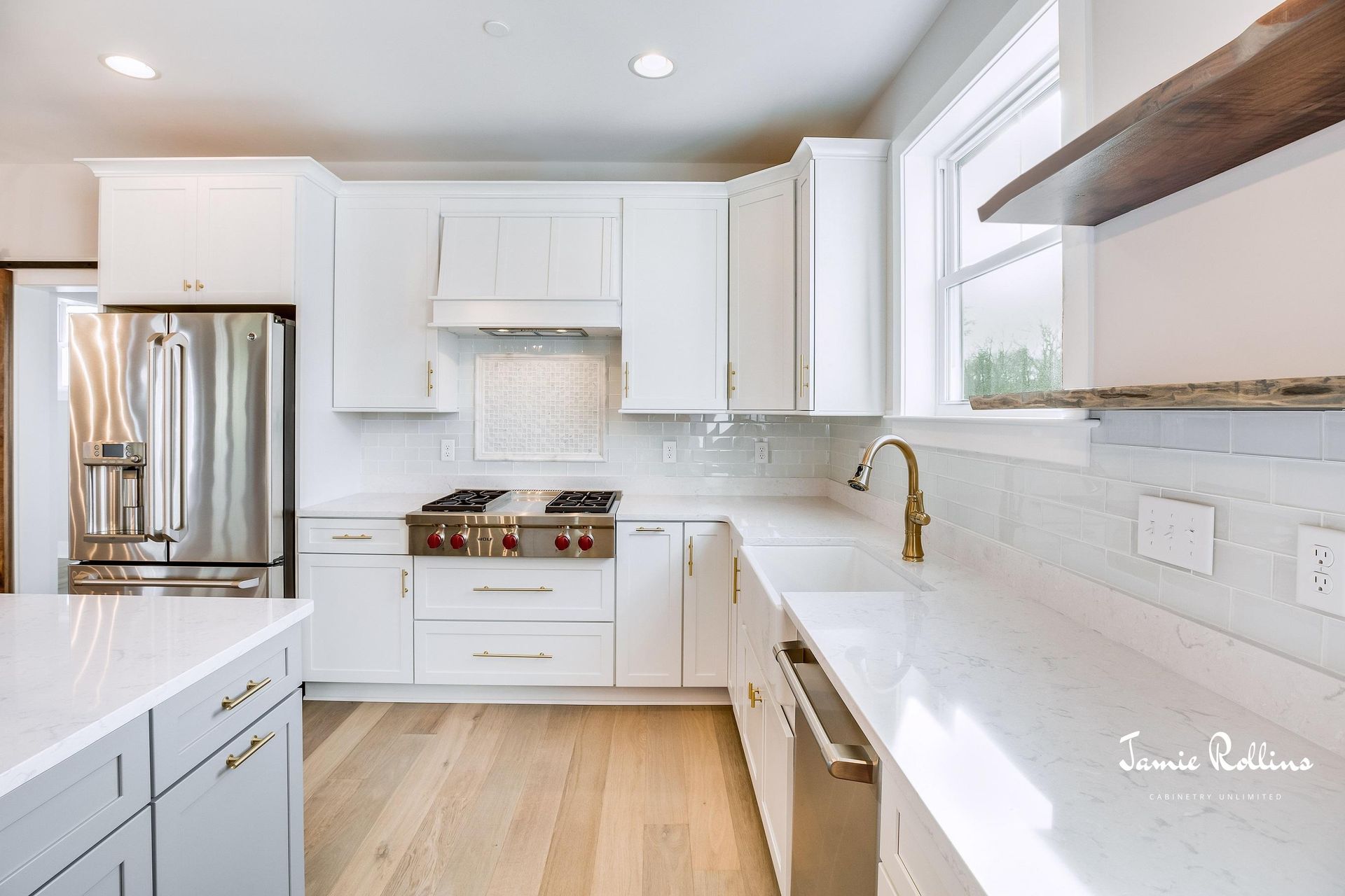 Modern white kitchen with stainless steel appliances, marble countertops, and wooden flooring.
