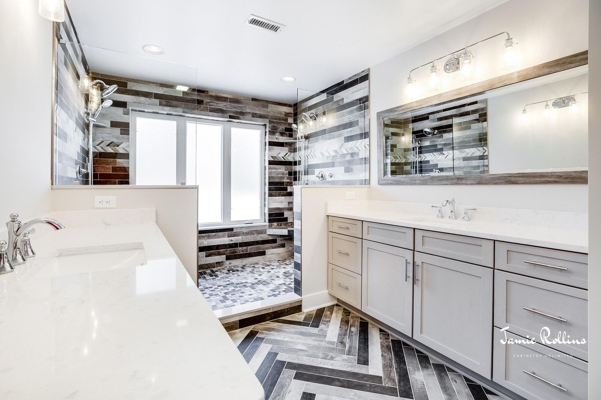 Modern bathroom with gray cabinets, a white countertop, and a shower with mixed-colored tile. Chevron-patterned floor.