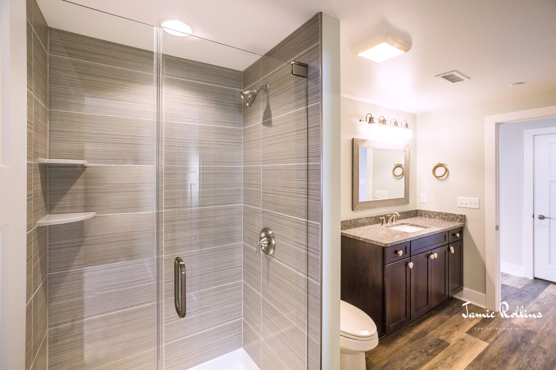 A modern bathroom featuring a glass shower with gray tile, a dark wood vanity, and a white toilet.
