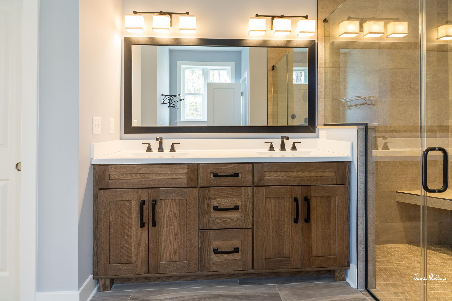 Bathroom with a wooden vanity, white countertop, large mirror, and a glass shower.