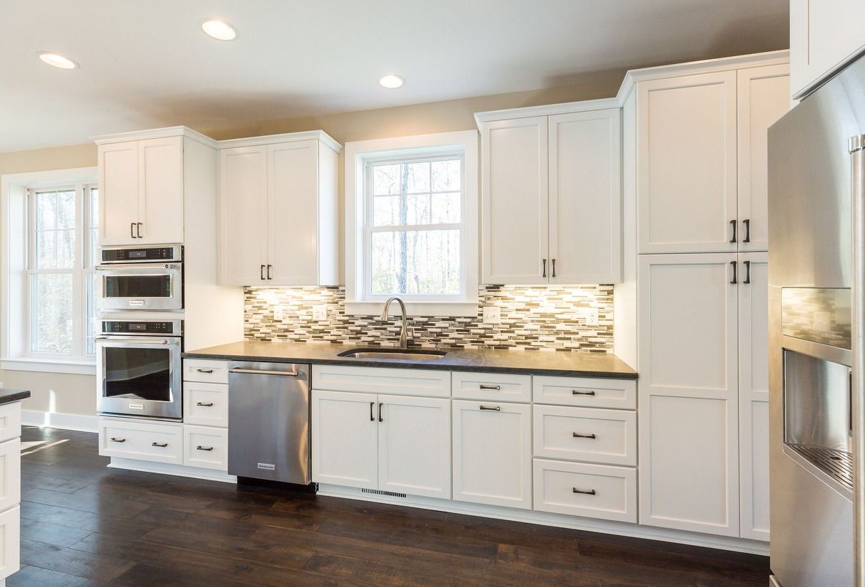 White kitchen with stainless steel appliances and dark countertops and floors. Cabinets and a window above the sink.