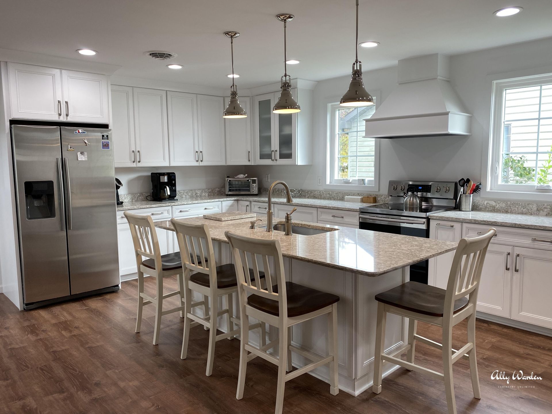 Modern white kitchen with island seating, stainless steel appliances, and pendant lights.