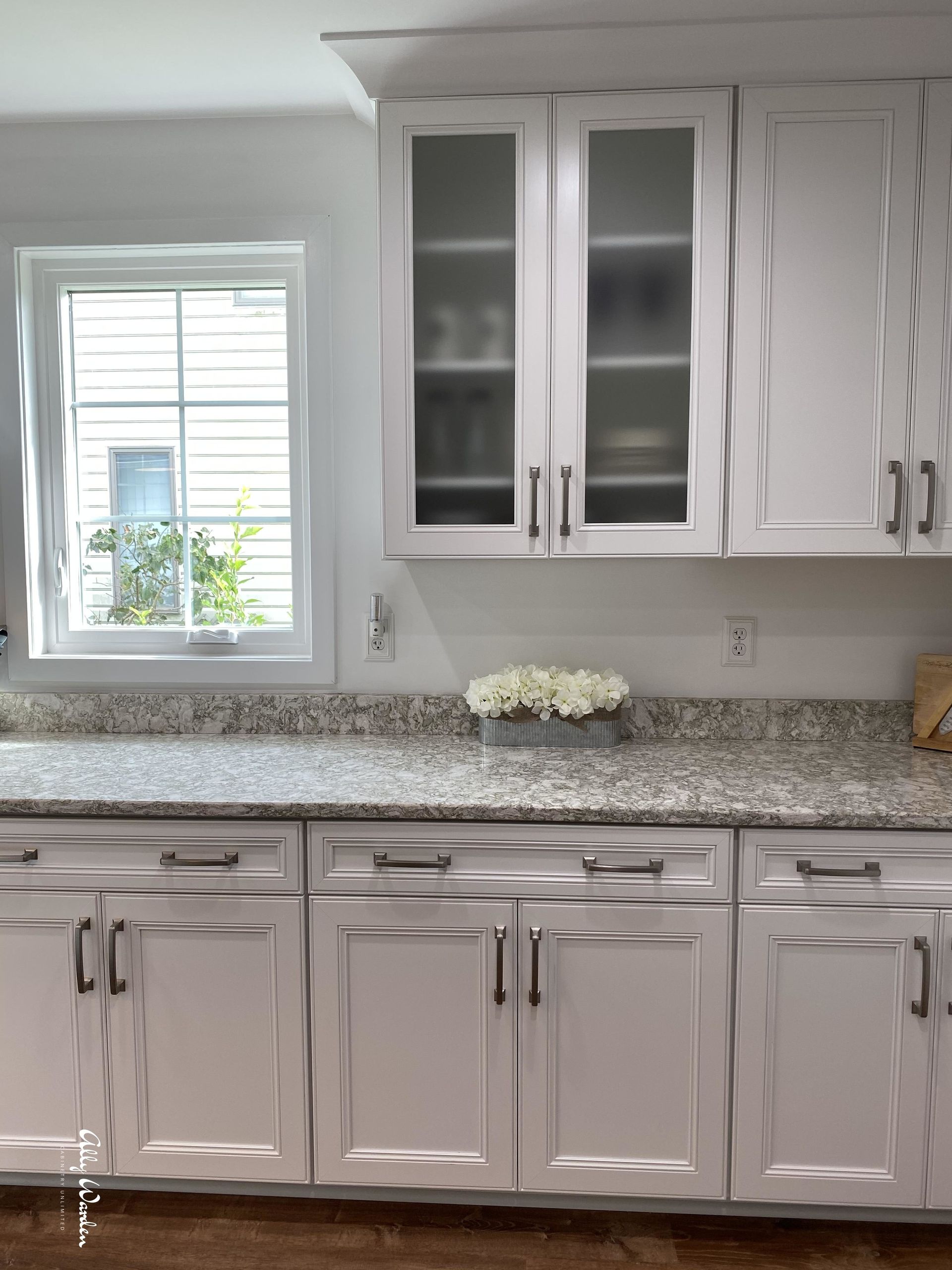 White kitchen cabinets with a light granite countertop and a window.