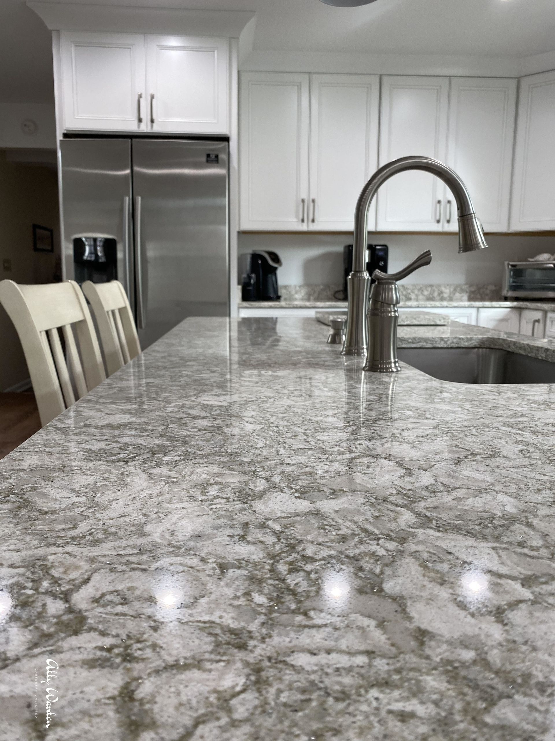 Kitchen with white cabinets, stainless steel refrigerator, and gray granite countertop. A silver faucet is on the island.