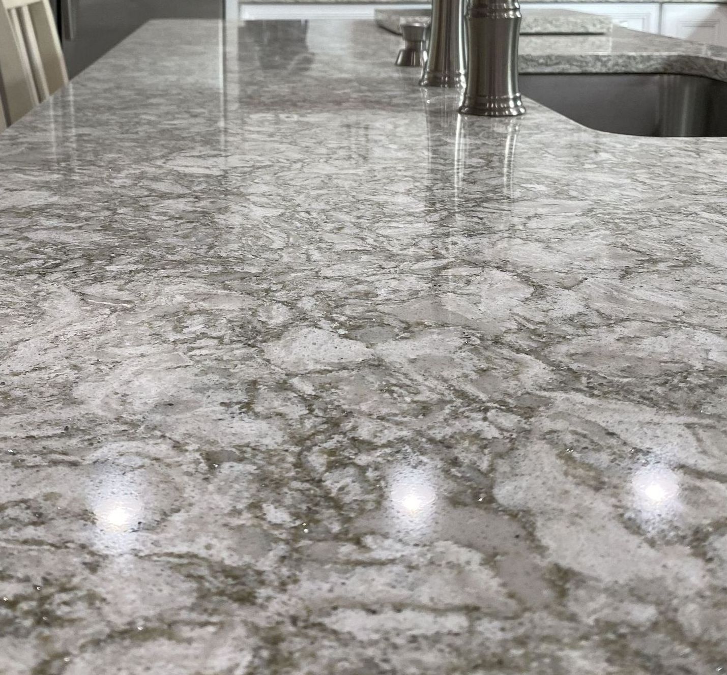 Close-up of a shiny white and gray marble countertop. A stainless steel faucet is in the background.