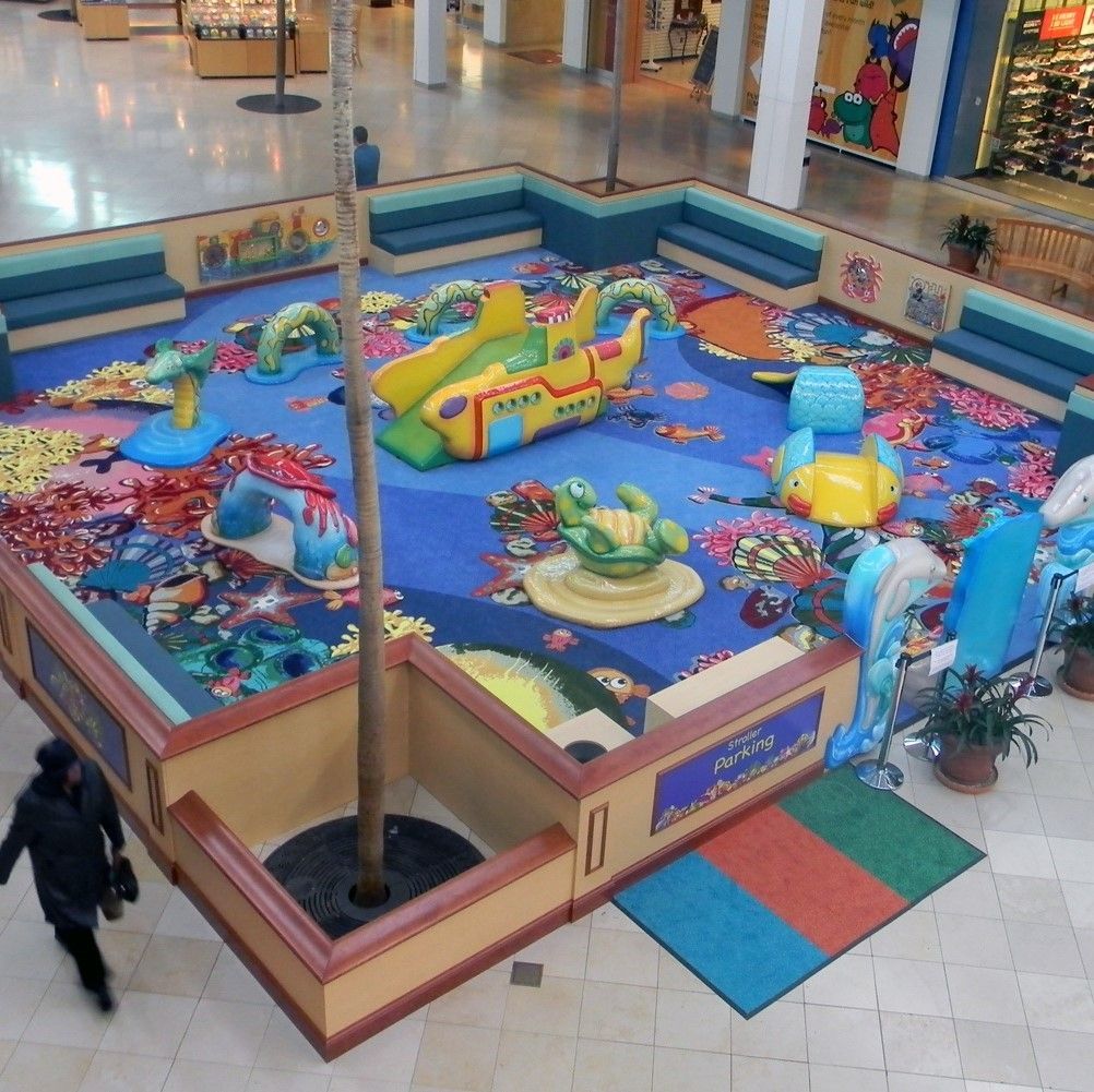 A children's play area in a mall, featuring sea-themed structures, padded seating, and a blue carpet.