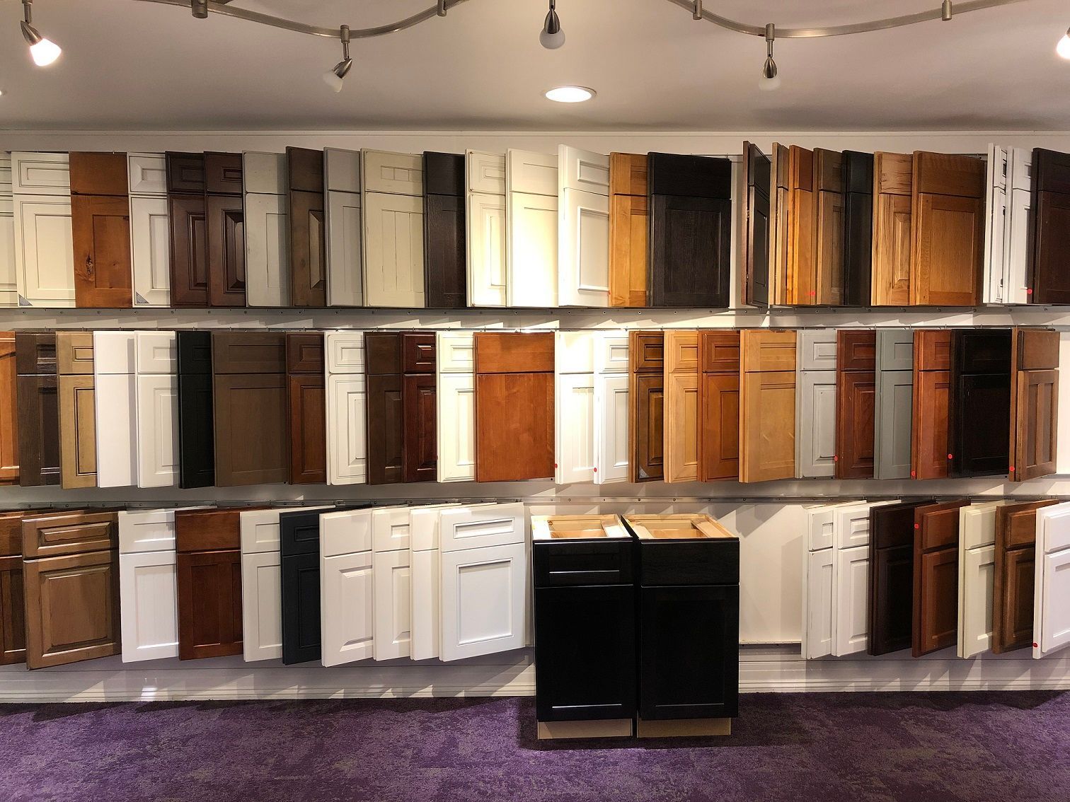 Cabinet door samples in various colors displayed on a wall in a showroom, with purple carpet below.