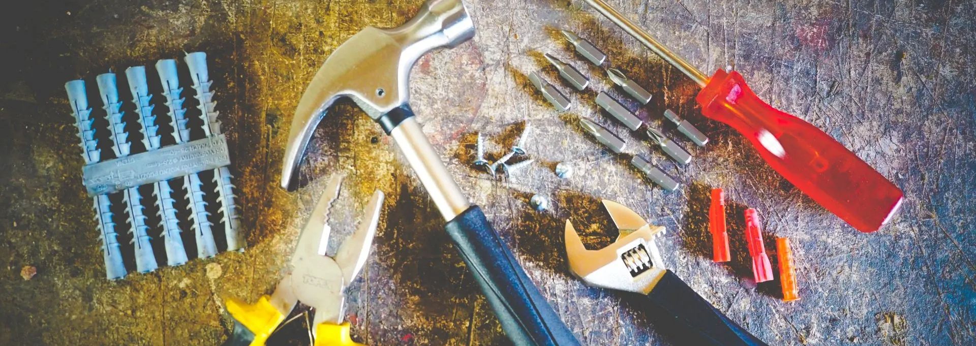 Various tools, including a hammer, pliers, screwdriver, and wrench, are arranged on a textured surface.