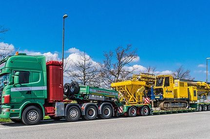 A green semi truck is carrying a yellow excavator on a trailer.