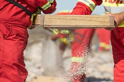 Two firefighters are cutting a piece of wood with a saw.