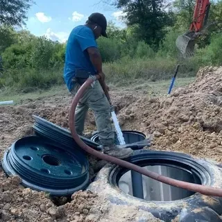 A man is pumping water into a septic tank with a hose.