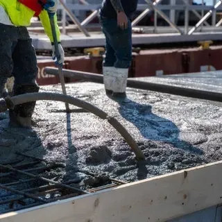 A construction worker is pouring concrete into a hole in the ground.
