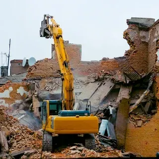 A yellow excavator is demolishing a brick building.