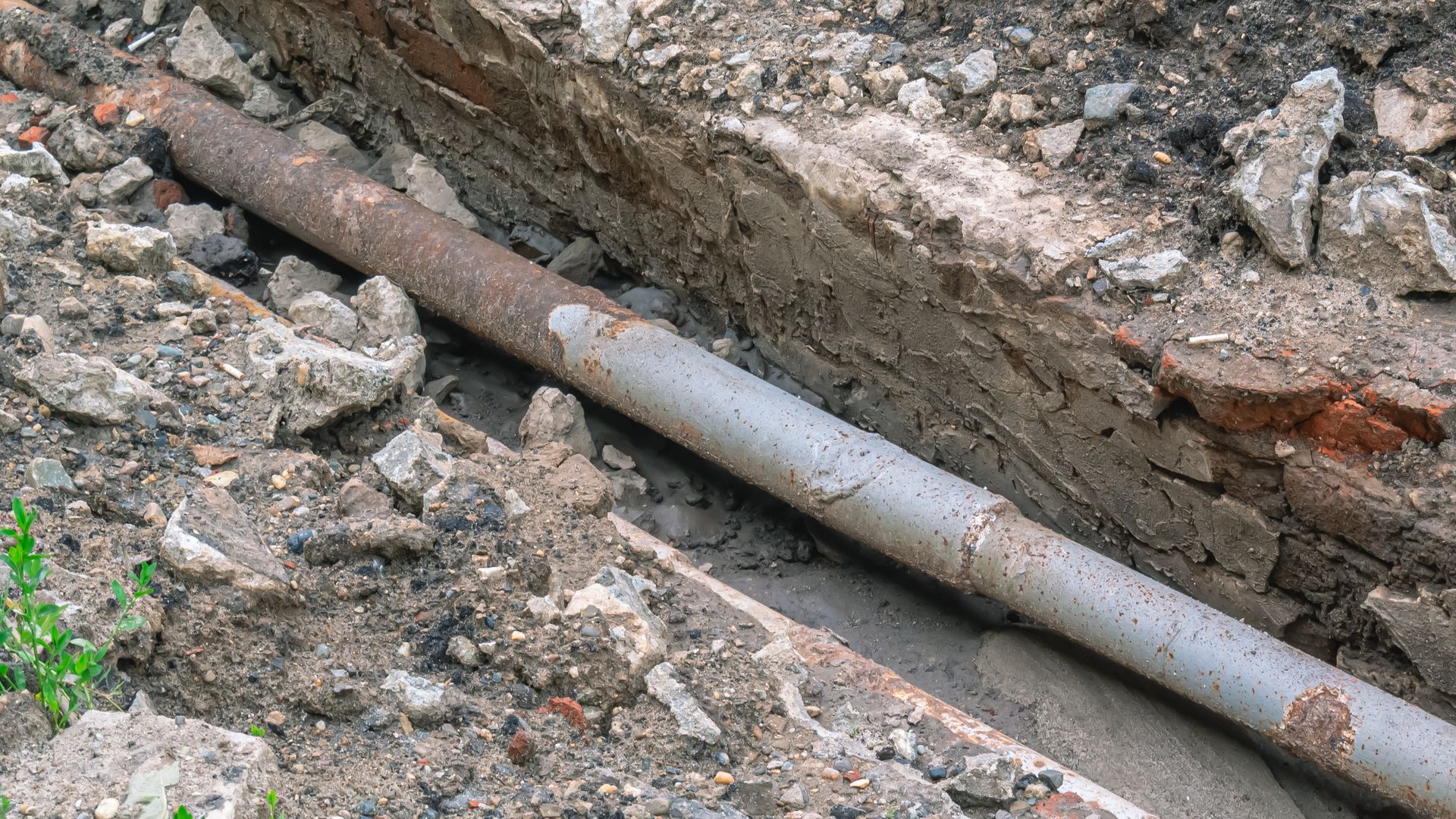 Exposed metal pipe running through a dirt trench with rocks and debris around it