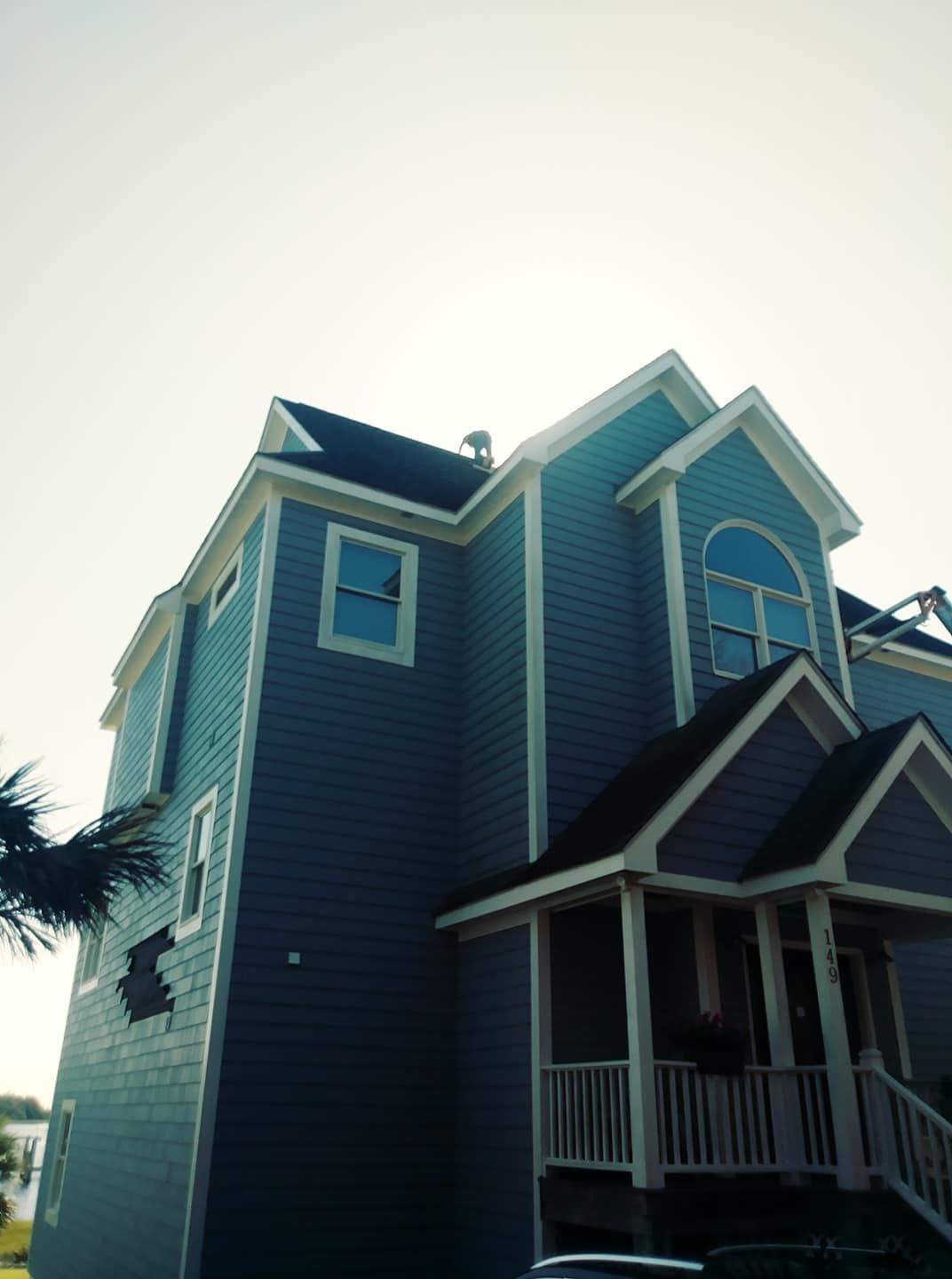 Blue two-story house with white trim; a porch, multiple windows, and gabled roof against a pale sky.
