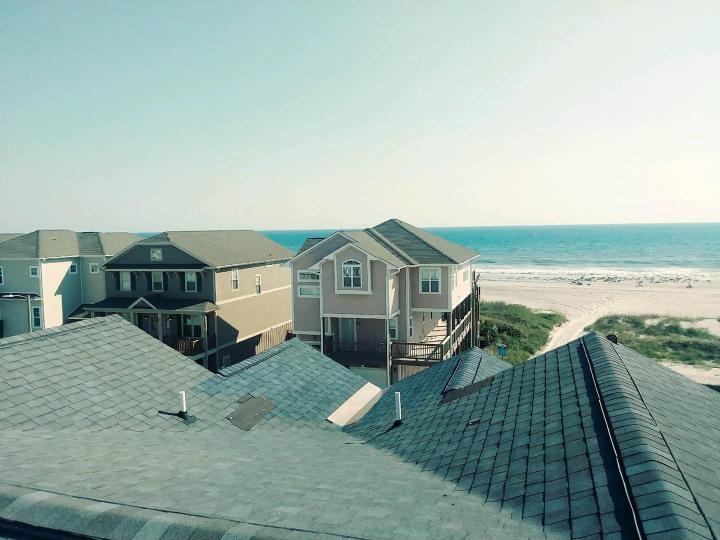 Rooftop view of houses overlooking a beach and ocean on a clear, sunny day.