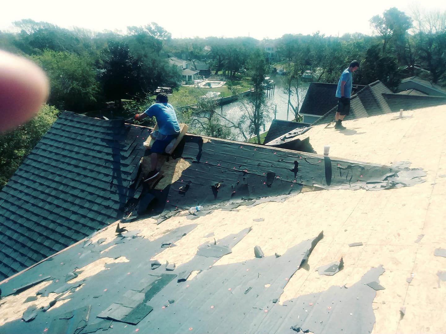 Two roofers removing old shingles on a sunny day.