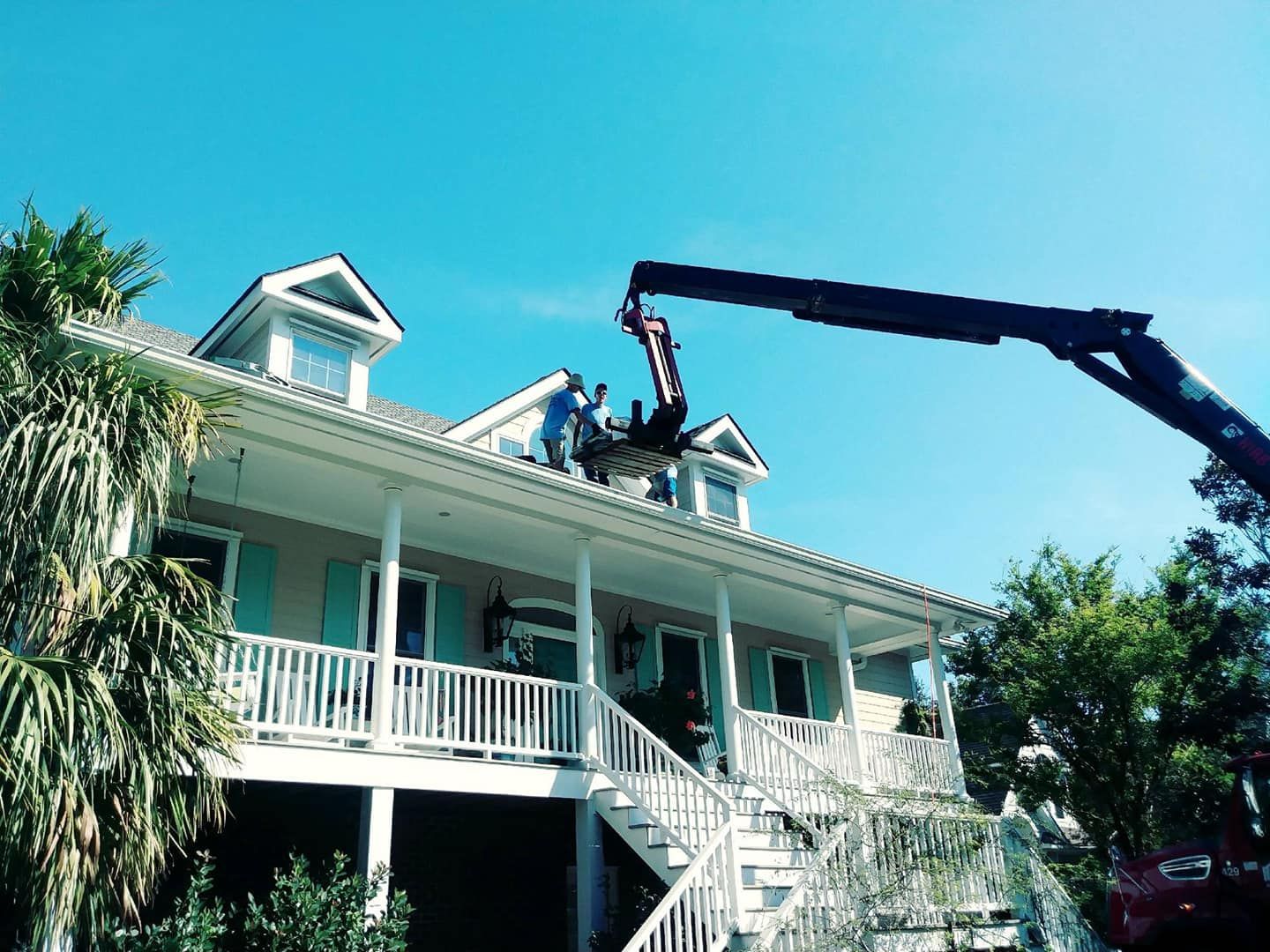 Workers on roof with crane removing debris, two-story house, blue sky.